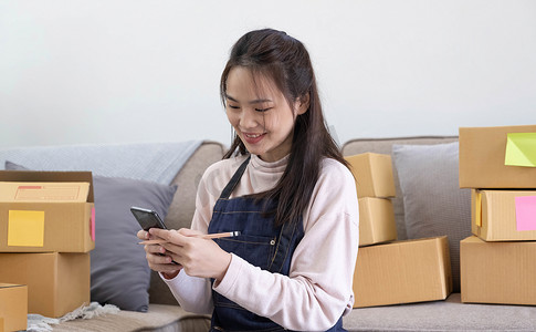 订单查看摄影照片_快乐的年轻亚洲女企业家，在家庭办公室用智能手机查看在线购物商店的订单后，为销售成功而微笑，在线商业和电子商务的概念