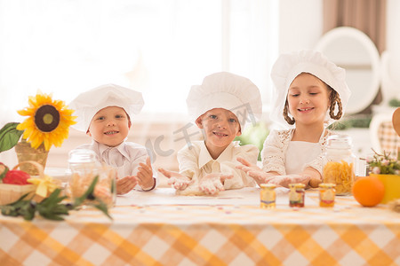 厨师面团摄影照片_以厨师的形式快乐的小孩在厨房里做美味的早餐