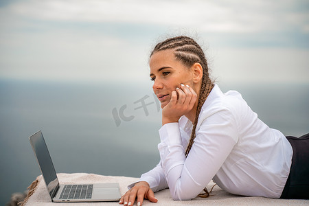 海边躺摄影照片_一位女士躺在露台上，在美丽海景的露台上用笔记本电脑键盘打字。