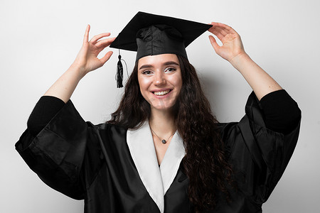拥有硕士学位的研究生女孩，穿着黑色毕业礼服，戴着白色背景的帽子。