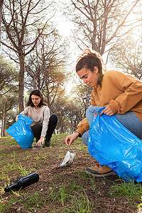 捡垃圾的人摄影照片_年轻的白人环保活动家妇女捡垃圾清理森林。