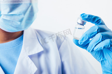 实验室专业科学家或医生手中拿着一小瓶 covid-19 疫苗，用白色背景的面罩手套和实验室外套进行治疗。
