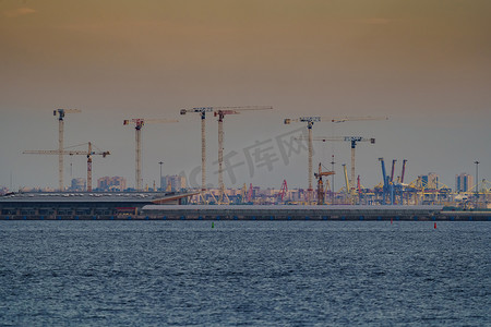 海港、建筑起重机和货港起重机在日落光下的海平线上