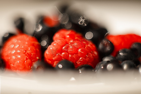 在明亮的阳光下，桌上的白色陶瓷盘子里放着许多多汁的鲜熟红草莓浆果