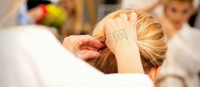 发型设计摄影照片_发型师的手在美容院为女性长发做专业发型设计。