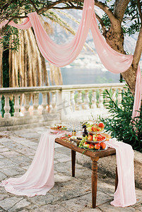 树下的石头露台上摆着带水果和眼镜的餐桌