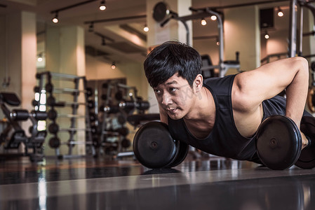 汗衫摄影照片_亚洲健身男子在健身房用哑铃进行推举运动的肖像。