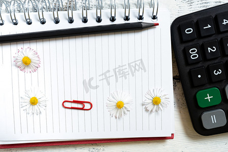 重要信息写在笔记本上，上面有鲜花、铅笔和夹在桌子上的计算器。