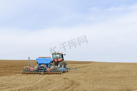 播种机器摄影照片_配备蓝色设备的红色拖拉机利用 GPS 导航在田间播种谷物，实现精准农业。