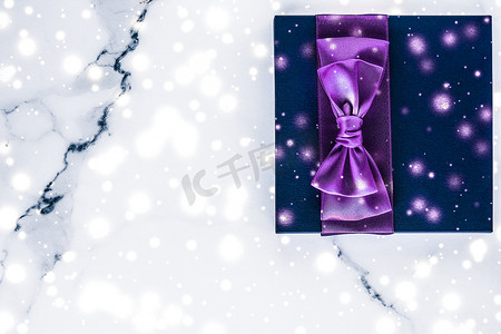 带紫色丝弓的寒假礼盒，大理石背景上闪闪发光的雪花，作为豪华美容品牌的圣诞和新年礼物，平面设计