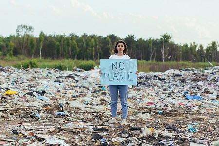 保护环境海报摄影照片_女志愿者在垃圾填埋场举着无塑料海报，积极分子与环境污染作斗争