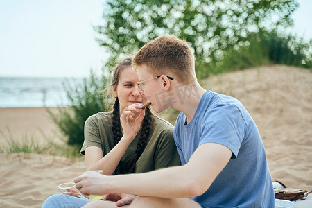 互相喂食摄影照片_年轻夫妇坐在海滩上互相喂食