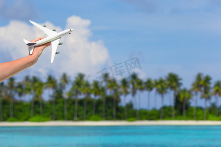 小飞机旅游摄影照片_人手中热带海滩上的小型白色玩具飞机