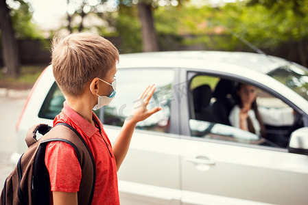 戴着医用口罩的小男孩在上学前在车里向母亲挥手告别