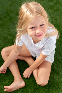 肖像漂亮微笑的金发女孩坐在绿草上。