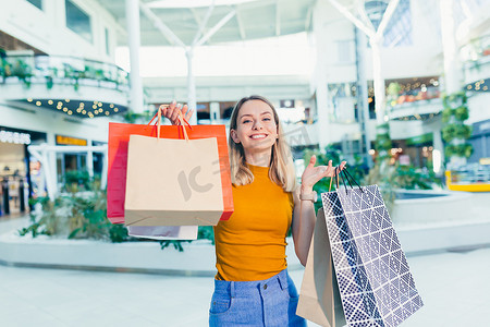 采集客户端摄影照片_开朗的年轻购物狂女人拿着装有购物品的纸袋，微笑着看着相机