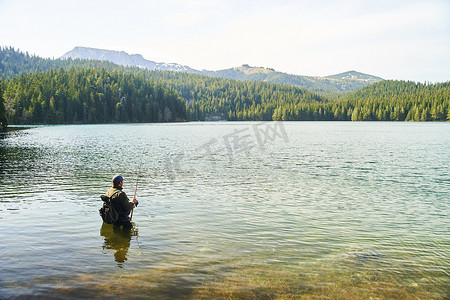 渔夫站在水里，在山的背景下在湖里抓鱼