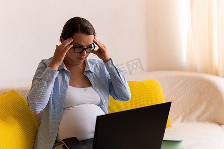 疲惫不堪、压力重重、心烦意乱的怀孕女商人带着笔记本电脑躺在沙发上。