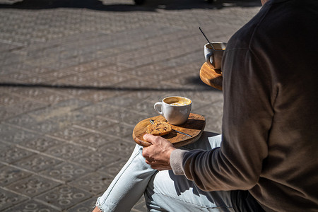 人们坐在街边的咖啡馆里，木盘上放着咖啡和饼干