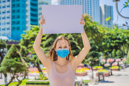 免费蓝色海报摄影照片_戴医用面具的妇女可以预防冠状病毒病，她拿着一张免费题词的海报。