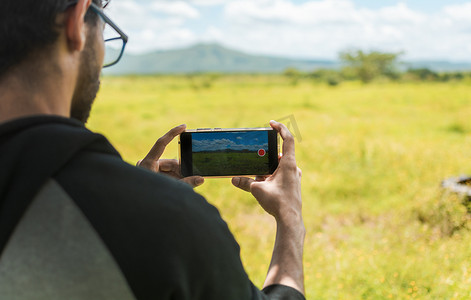 男子双手用手机拍摄风景照片的特写。