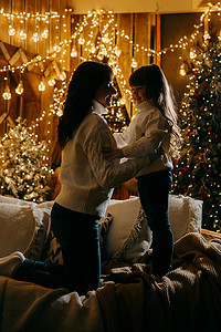 一个小女孩和她的母亲在舒适的家庭环境中，坐在圣诞树旁边的沙发上。