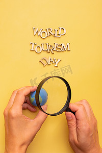 假期旅游海报摄影照片_黄色背景上的木制字母的世界旅游日文字，女性手中有地球仪和放大镜
