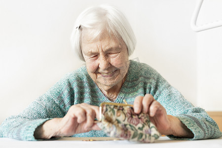 开朗的 96 岁老妇人坐在家里的餐桌旁，支付账单后，她对钱包里的养老金储蓄感到满意。