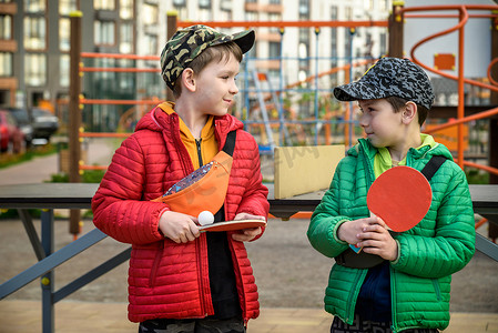 两个快乐的男孩，十几岁的双胞胎兄弟，在户外享受假期打乒乓球。