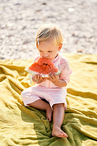 小女孩在圆石滩上的毯子上吃西瓜