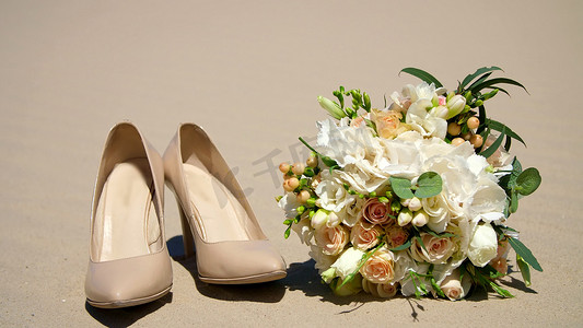 夏天，沙漠，婚礼女性米色高跟鞋站在沙子上，旁边是婚礼花束。