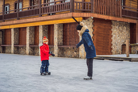 年轻的母亲教她的小儿子在室外溜冰场滑冰。