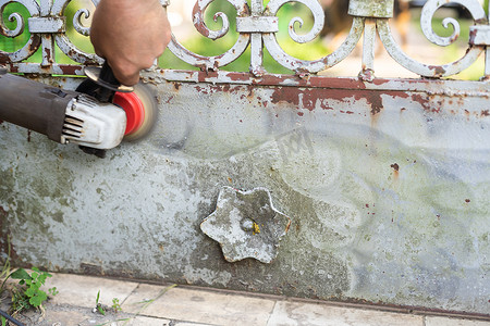 杂工从生锈的栅栏上刮掉旧油漆