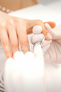 美容院美甲师用美甲剪刀的特写去除女性指甲的角质层。