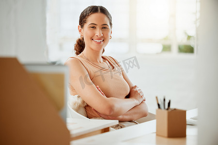 一位自信的年轻西班牙裔女商人在办公室工作时双臂交叉坐着的肖像。