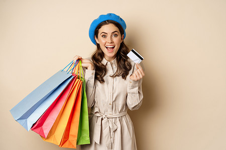 时尚女性女孩的画像，摆着商店和信用卡的购物袋，非接触式支付，打折购买，米色背景