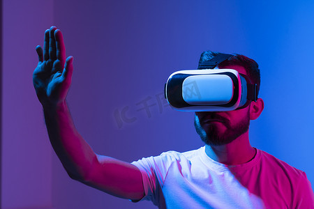 年轻男子游戏玩家使用虚拟现实耳机并与朋友在元宇宙中玩最喜欢的视频游戏的肖像。 