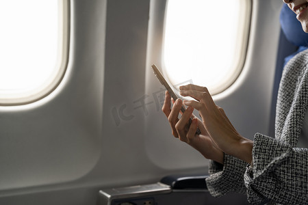 年轻女商人在飞机上使用智能手机的侧视图，嬉皮士拿着移动设备在飞行中玩耍或工作，商务旅行概念