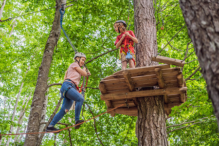母亲和儿子在森林里的极限公路电车滑索上攀登树上的登山绳安全连接到树顶绳索冒险公园。