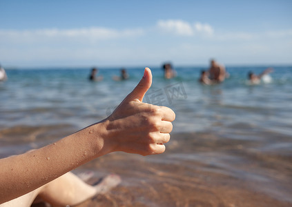 女性手竖起大拇指在海和天空背景特写。
