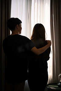人拥抱剪影摄影照片_在家里窗户对面的客厅里，一对年轻夫妇相拥而立的剪影。