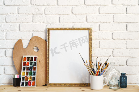 相框作为画架，木桌上有艺术家的工具，靠在白砖墙上
