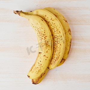 皮肤斑点摄影照片_亮白木桌上有棕色斑点的成熟香蕉