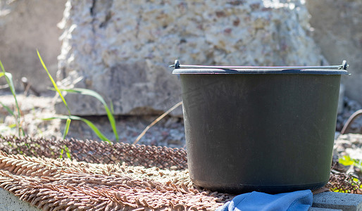 塑料桶摄影照片_夏季花园里装水的黑色塑料桶。