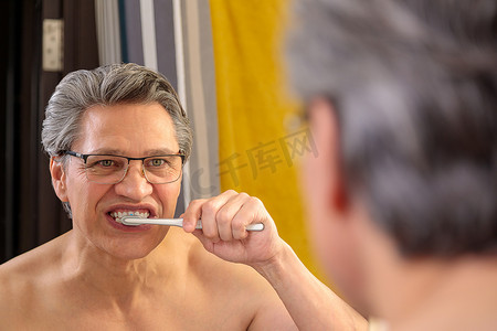 一个头发灰白的成年男子用牙刷刷牙，照镜子