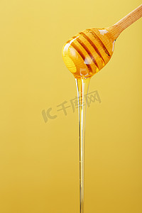 黄色背景中的木制蜂蜜浸渍器中滴出金色的蜂蜜