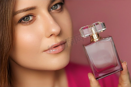 香水广告摄影照片_粉红色背景的香水、美容产品和化妆品模特脸部肖像，美丽的女人拿着带有花卉女性香味、时尚和化妆的香水瓶