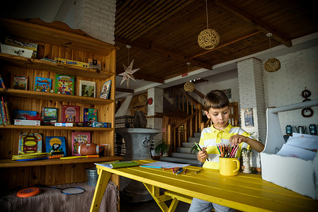 小可爱的卷发男婴坐在书架旁边的生态客厅内部的地板上，在专辑中用彩色毡尖笔画画。