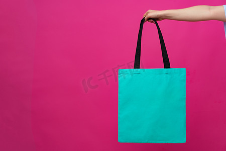 粉红色背景下女性手持生态或可重复使用的购物袋