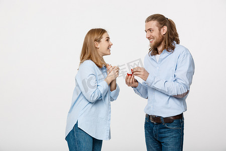 提案概念-男人在孤立的白色背景下向他美丽的女朋友展示订婚戒指钻石的肖像。